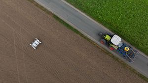 Aus der Vogelperspektive: Ein Roboter auf einem Feld, ein Weg, auf dem ein Traktor fährt.