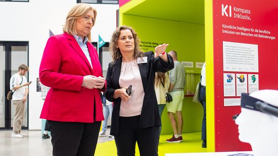 Susan Beudt, stellvertretende Leiterin des Educational Technology Lab am DFKI und Konsortialleiterin des Projekts KI-Kompass Inklusiv (r.) erläutert Bundesministerin Bärbel Bas (l.), wie KI-gestützte Assistenztechnologien Menschen mit Behinderungen im Arbeitsleben unterstützen können