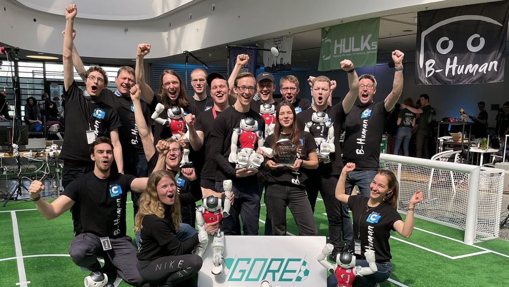 Teamfoto: jubelndes B-Human Team mit Robos und Pokal